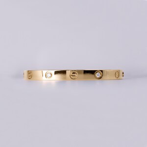 May include: A gold bangle bracelet with a polished finish and small clear diamonds set into the band.