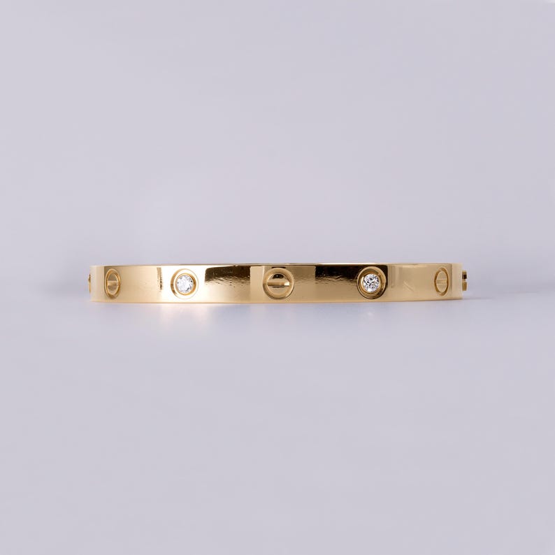 May include: A gold bangle bracelet with a polished finish and small clear diamonds set into the band.