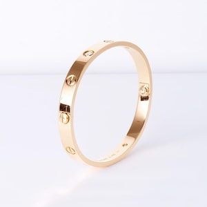 May include: A gold bangle bracelet with a diamond set in the center. The bracelet is decorated with screws around the edge. The bracelet is made by Cartier and has the inscription 'Cartier 750' on the inside.