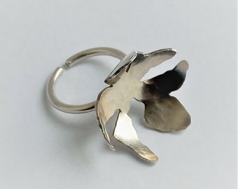 May include: A silver ring with a flower-shaped design. The ring is made of metal and has a smooth finish.