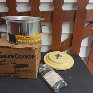 May include: A silver Wear-Ever Bounty pressure cooker with a yellow label, a matching yellow lid, and a cardboard box labeled Pressure Cooker. The box displays the text 1 No. H3614 4 qt. and includes a plastic-wrapped accessory component.