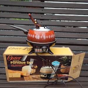 May include: An orange Oster electric fondue pot with a black base, a long handle, and a white geometric pattern around the center. The pot includes several fondue forks and sits atop its original cardboard box labeled Oster Electric Fondue Set.