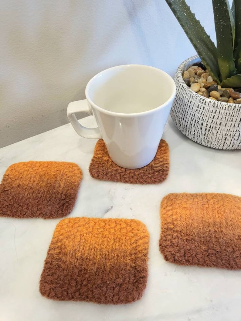 Orange variegated set of 4 square wool coasters, with mug sitting on top of one of the coasters.