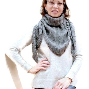 K&ouml;nnte beinhalten: Eine Frau tr&auml;gt einen grauen Strick Schal, einen wei&szlig;en Pullover und eine blaue Jeans. Sie steht vor einem wei&szlig;en Hintergrund.