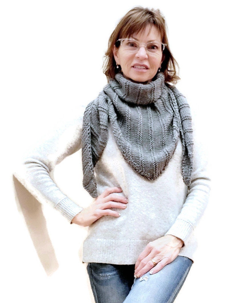 K&ouml;nnte beinhalten: Eine Frau tr&auml;gt einen grauen Strick Schal, einen wei&szlig;en Pullover und eine blaue Jeans. Sie steht vor einem wei&szlig;en Hintergrund.