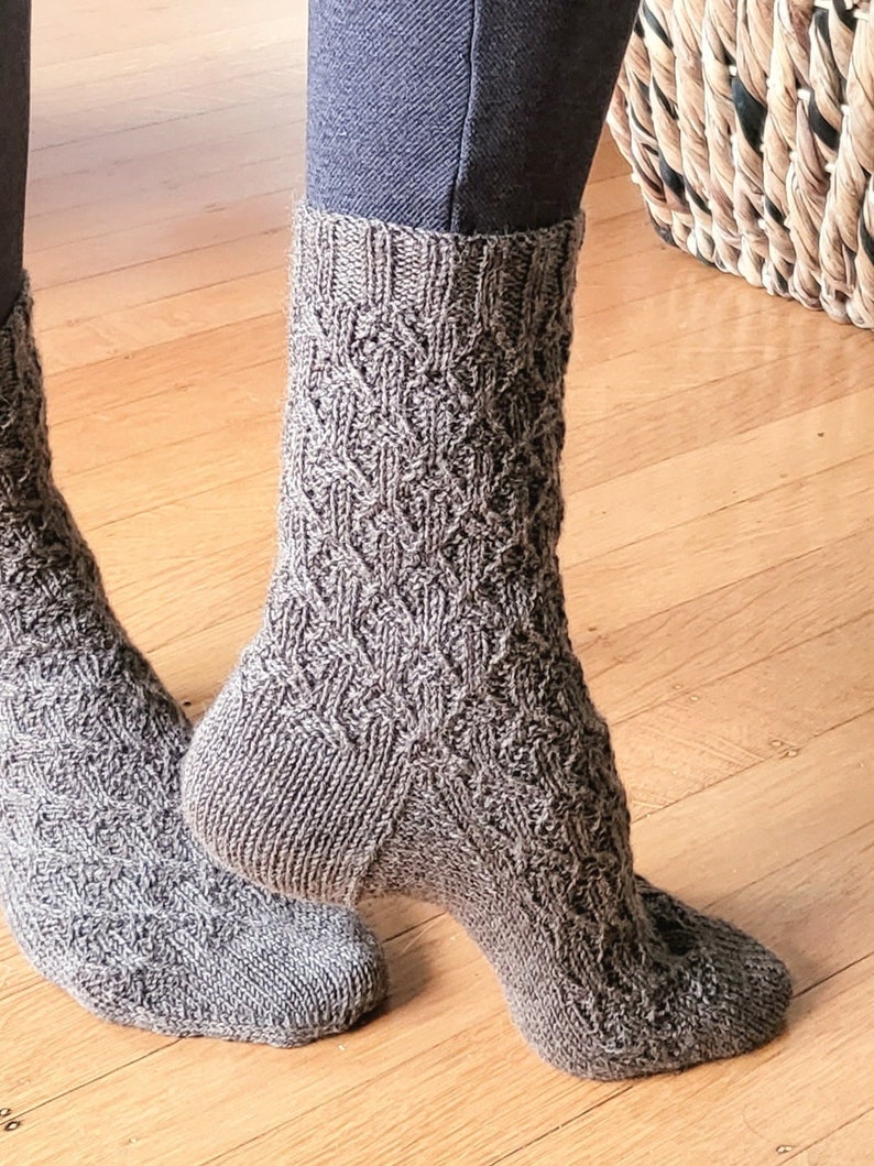 May include: A pair of brown knitted socks with a cable knit pattern. The socks are worn on a person's feet.