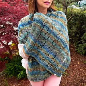 Pode incluir: Um xale de malha azul, verde e dourado com um padrão de renda. O xale está drapeado sobre os ombros de uma pessoa.