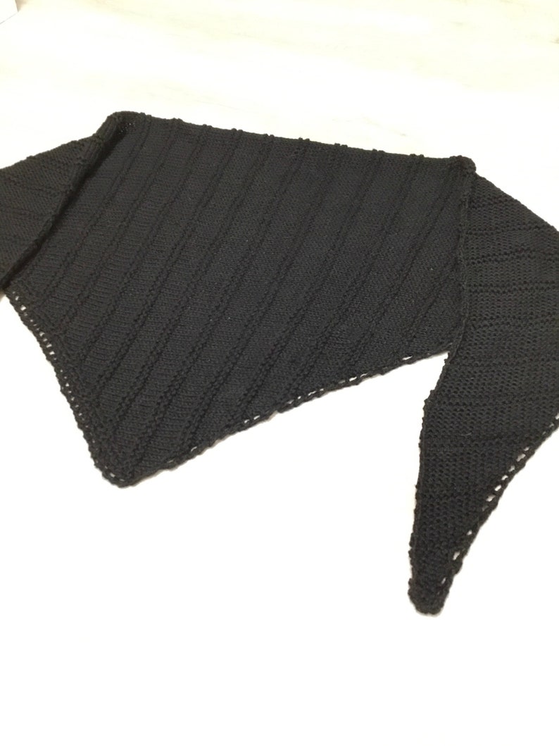 K&ouml;nnte beinhalten: Ein schwarzer gestrickter Schal mit dreieckiger Form und einem strukturierten Muster.