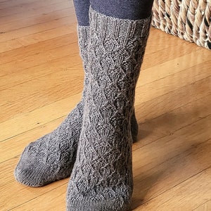 May include: A pair of brown knitted socks with a cable knit pattern. The socks are worn on a person's feet.