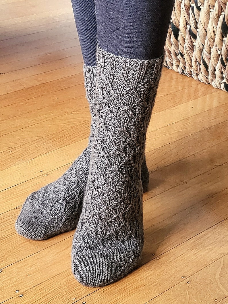 May include: A pair of brown knitted socks with a cable knit pattern. The socks are worn on a person's feet.