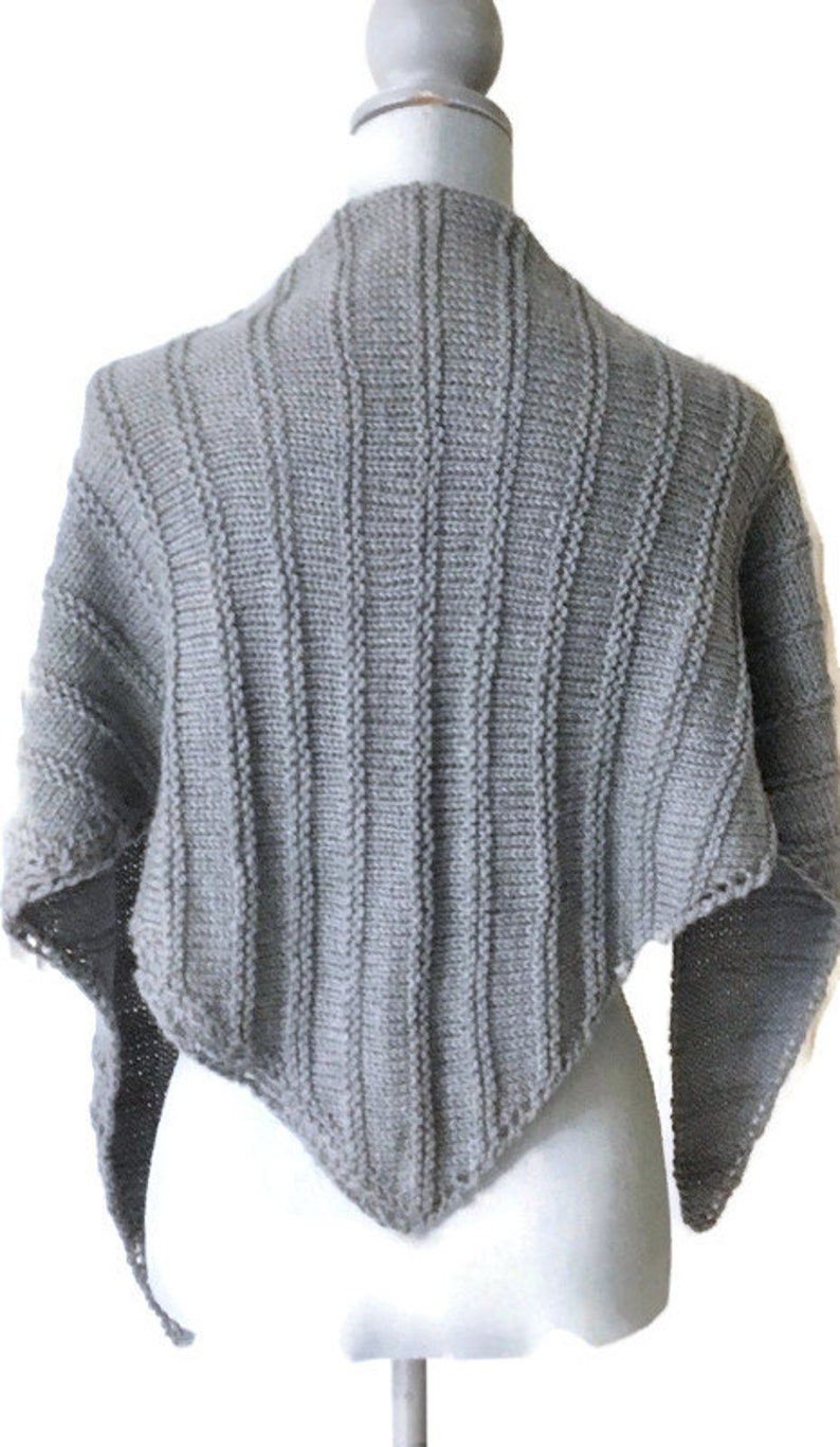 K&ouml;nnte beinhalten: Ein grauer, gestrickter, dreieckiger Schal mit Rippenstruktur. Der Schal ist &uuml;ber eine wei&szlig;e Schaufensterpuppe gelegt.