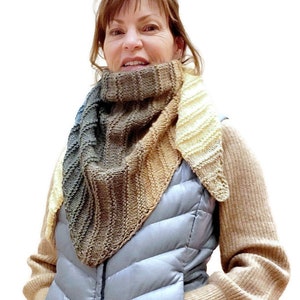 K&ouml;nnte beinhalten: Eine Frau tr&auml;gt einen braunen, beige und cremefarbenen Strickschal mit einer grauen Steppweste und einem braunen Pullover.