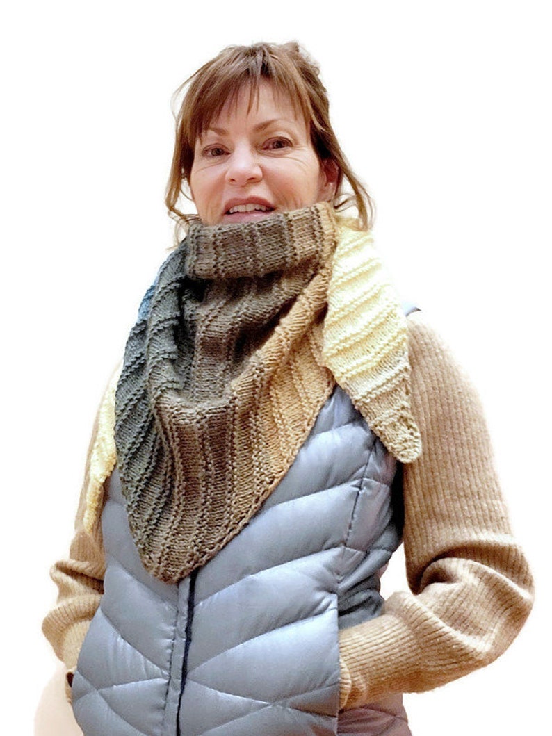 K&ouml;nnte beinhalten: Eine Frau tr&auml;gt einen braunen, beige und cremefarbenen Strickschal mit einer grauen Steppweste und einem braunen Pullover.