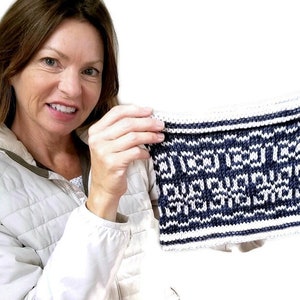 May include: A close-up of a knitted fabric swatch with a geometric pattern in white and navy blue. The fabric is held by a person's hands.