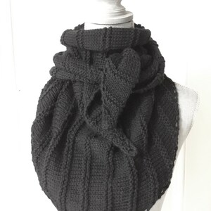 K&ouml;nnte beinhalten: Ein schwarzer Strick Schal mit einem einzigartigen Design. Der Schal ist gefaltet und &uuml;ber eine wei&szlig;e Schaufensterpuppe gelegt.