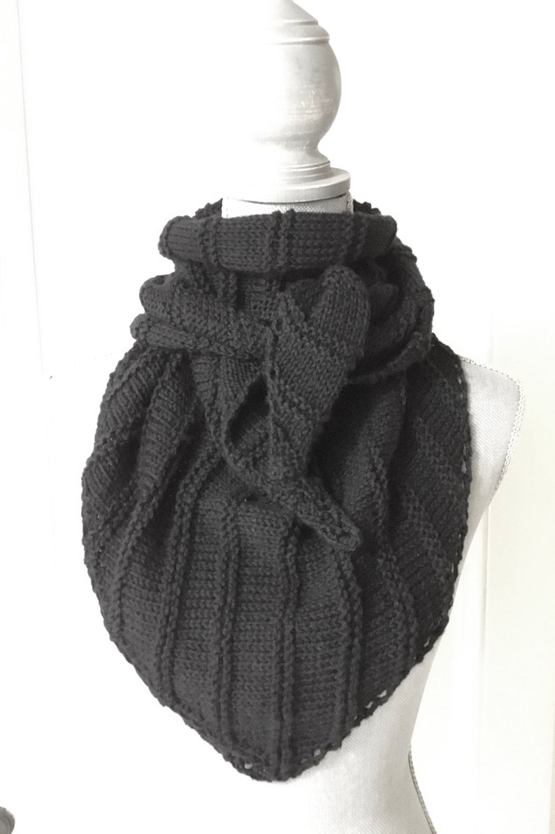 K&ouml;nnte beinhalten: Ein schwarzer Strick Schal mit einem einzigartigen Design. Der Schal ist gefaltet und &uuml;ber eine wei&szlig;e Schaufensterpuppe gelegt.
