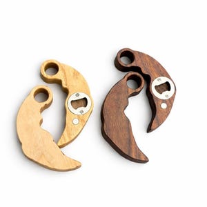 May include: Four wooden bottle openers in light and dark wood tones. Each opener has a curved handle with a circular opening and a metal bottle cap opener. The openers are arranged on a white background.