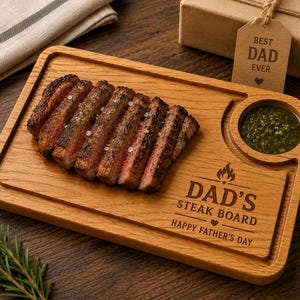 May include: A rectangular wooden serving board with a carved circular dip containing green sauce. The board is engraved with the text DAD'S STEAK BOARD HAPPY FATHER'S DAY and a flame icon. Sliced grilled steak is arranged on the board surface.