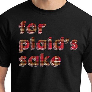 May include: Black t-shirt with the phrase "for plaid's sake" in red, yellow, and white plaid lettering. The shirt has a crew neck and short sleeves. The text is in a bold, playful font.
