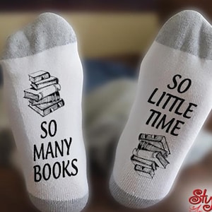 May include: A pair of white socks with black text. One sock says "So many books" and has a drawing of a stack of books. The other sock says "So little time" and also has a drawing of a stack of books.
