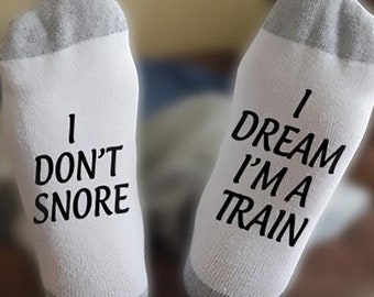 May include: A pair of white socks with grey heels and toes. One sock says "I don't snore" and the other says "I dream I'm a train".