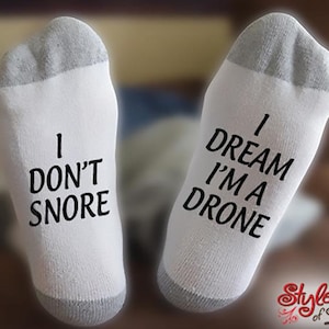 May include: A pair of white socks with gray trim. One sock says "I don't snore" and the other says "I dream I'm a drone".
