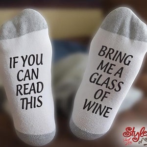 May include: White socks with black text. One sock reads "If you can read this" and the other sock reads "Bring me a glass of wine".