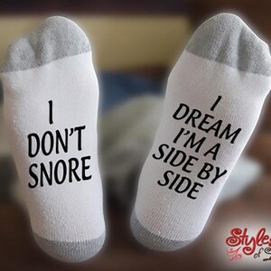May include: A pair of white socks with black text. One sock says "I don't snore" and the other sock says "I dream I'm a side by side".