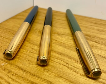 May include: Three gold-toned fountain pens with different colored barrels: blue, black, and green.