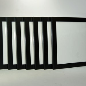 May include: Eight black picture frames of various sizes are lined up in a row. The frames are all made of wood and have a simple, modern design.