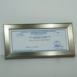 May include: A silver framed certificate with blue text. The text reads "Department of Professional and Occupational Regulation Commonwealth of Virginia Board for Barbers and Cosmetology Cosmetologist License Display in Plain View of Public Rockville, MO 20052"