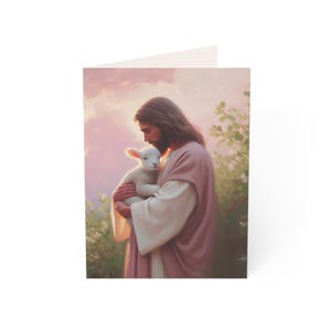 May include: A greeting card featuring a painting of a man with long brown hair and a beard, wearing a pink robe, cradling a white lamb. The background shows a soft pink sky and green foliage.