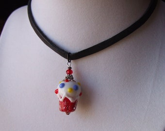 May include: A black leather choker necklace with a red, white, and blue glass cupcake charm. The cupcake has yellow and blue sprinkles.