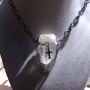 May include: A silver chain necklace with a large clear quartz crystal pendant and a small silver cross charm.
