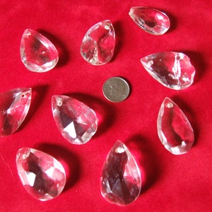 Puede incluir: Diez prismas de cristal transparentes en forma de l&aacute;grima con un dise&ntilde;o facetado, presentados sobre una superficie de terciopelo rojo.