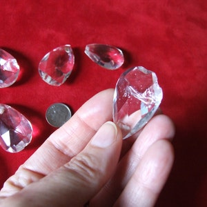 Puede incluir: Una colecci&oacute;n de colgantes de cristal transparente en forma de l&aacute;grima. Los colgantes son facetados y tienen un alto brillo. Se muestran sobre una superficie de terciopelo rojo.