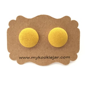 Op de afbeelding: Een paar gele stoffen knoop oorbellen getoond op een bruine kaart met de tekst "www.mycookiejar.com".
