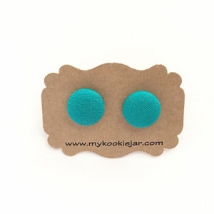 May include: A pair of turquoise fabric button earrings on a brown card with the text "www.mycookiejar.com".