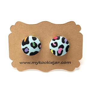 May include: A pair of blue and black fabric stud earrings with a colourful leopard print design. The earrings are displayed on a brown card with the website address "www.mykooklejar.com".