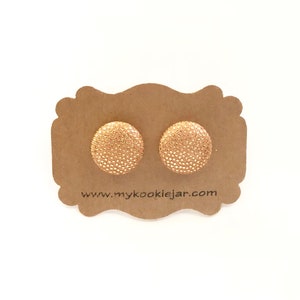 May include: A pair of gold stud earrings with a textured surface. The earrings are displayed on a brown card with the website address "www.mycookiejar.com".