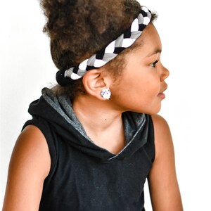 May include: A young person with curly hair wearing a black sleeveless hoodie with a grey hood and a black and white braided headband.