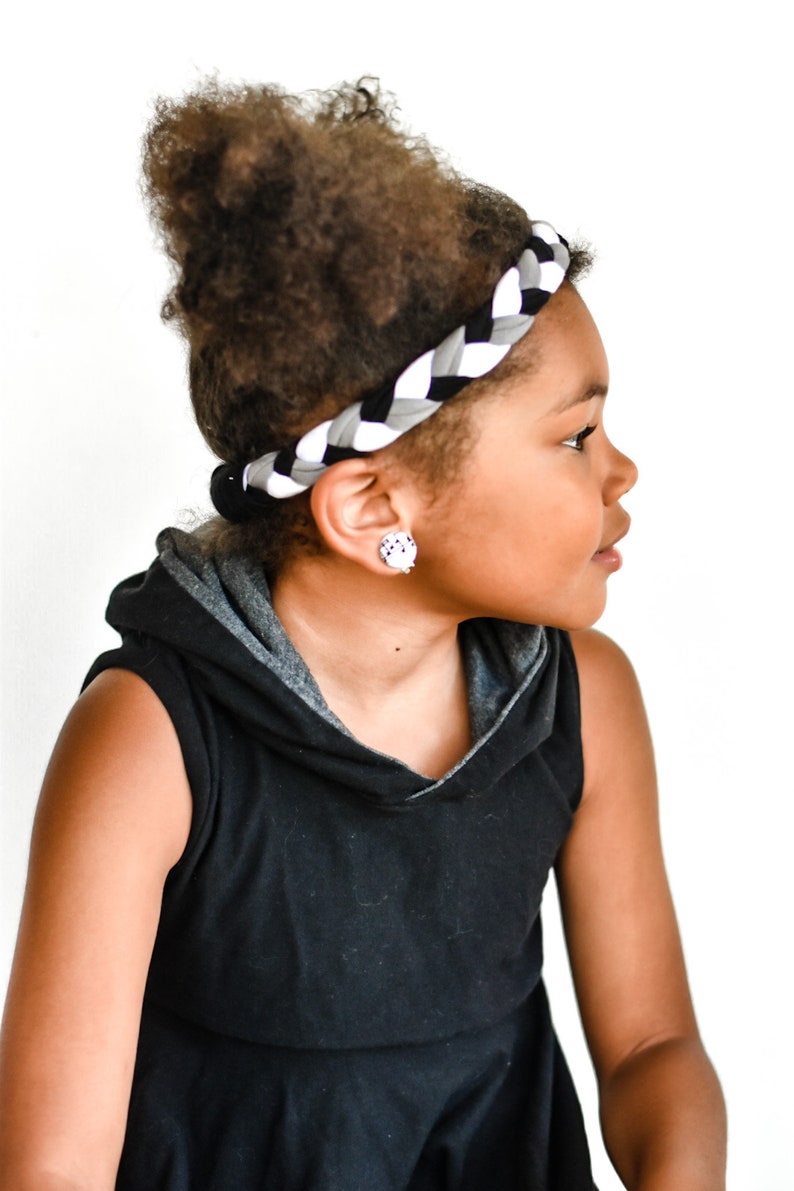 May include: A young person with curly hair wearing a black sleeveless hoodie with a grey hood and a black and white braided headband.