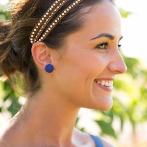 May include: A woman wearing a headband with a blue circle stud earring. The earring is made of a textured material.