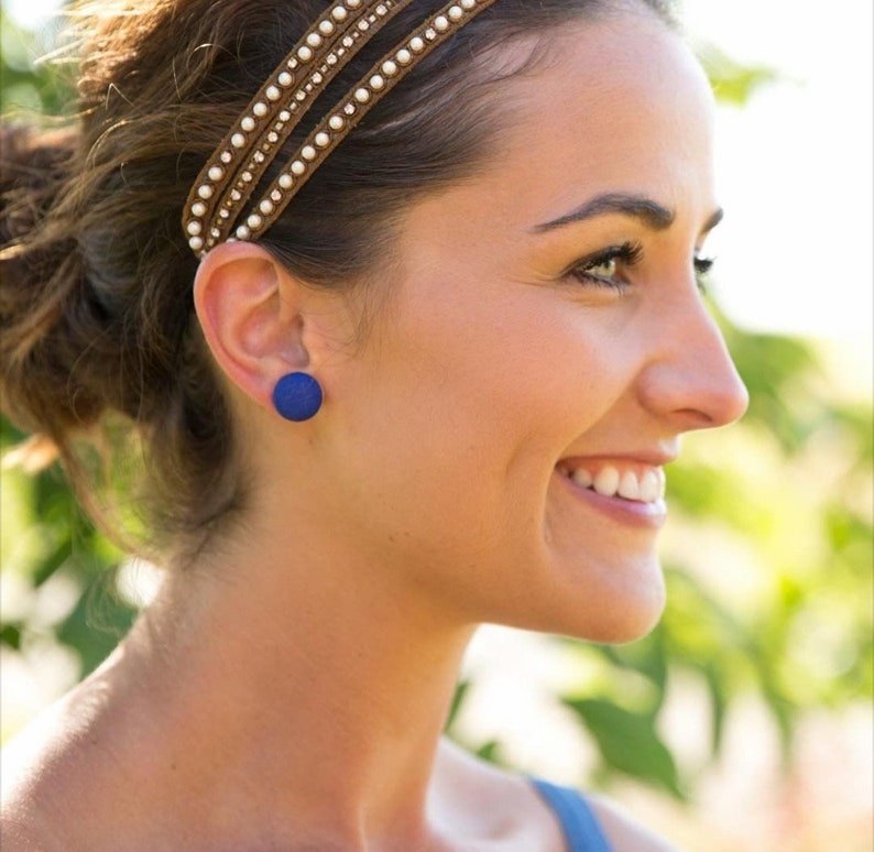 May include: A woman wearing a headband with a blue circle stud earring. The earring is made of a textured material.