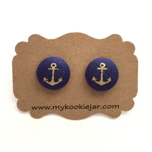 May include: A pair of navy blue fabric earrings with gold anchor designs. The earrings are displayed on a brown card with the website address "www.mycookiejar.com".