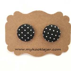 Puede incluir: Un par de pendientes de botón de tela con lunares negros y blancos. Los pendientes se muestran en una tarjeta marrón con el sitio web www.mycookiejar.com impreso en ella.