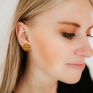 May include: A pair of round stud earrings with a yellow and black checkered pattern.