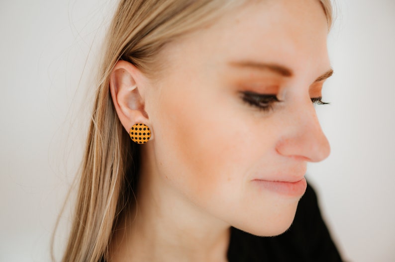 May include: A pair of round stud earrings with a yellow and black checkered pattern.