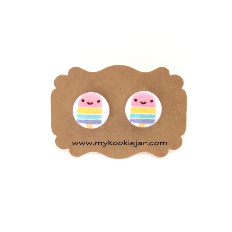 May include: A pair of colorful popsicle stud earrings with a smiling face on each. The earrings are on a brown card with the text "www.mycookiejar.com".