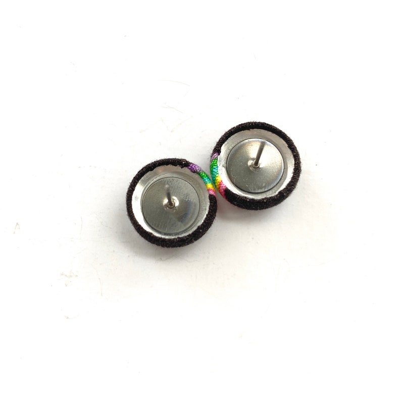 May include: A pair of brown fabric earrings with rainbow colored thread accents. The earrings have silver posts and backs.